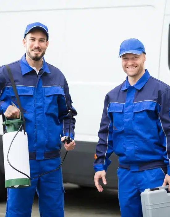 Two smiling pesticide workers in blue uniforms holding tools, standing in front of a white van.