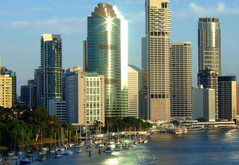 Waterfront cityscape with modern skyscrapers and numerous boats moored in the harbor under a clear blue sky.