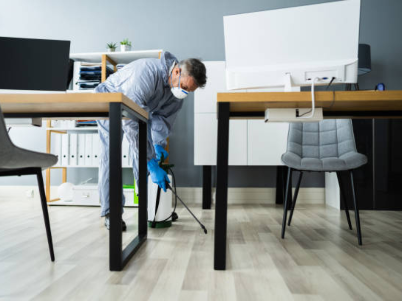 Man in protective mask and gloves uses a swab and test tube to collect samples from an office environment.